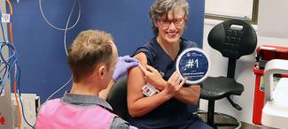 Registered Nurse, Rachel holds a sign saying '1st COVID vaccination' at Lismore Base Hospital. 